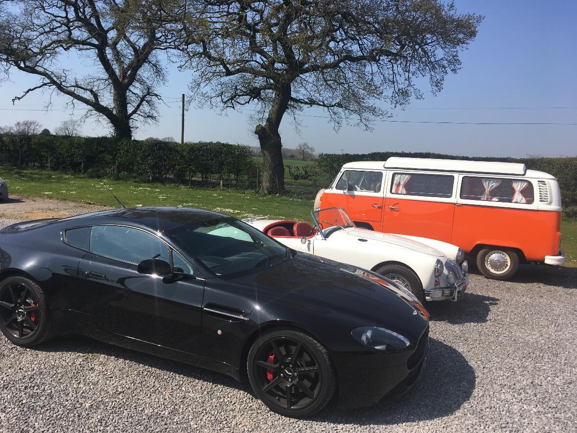 Outside our beautiful storage facility countryside location showcasing a black sports car, a white classic car and an orange classic camper van.