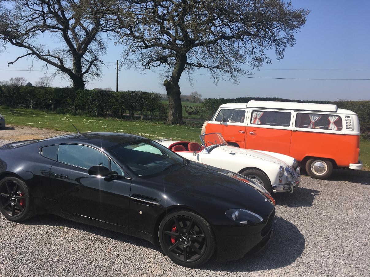 Outside our beautiful storage facility countryside location showcasing a black sports car, a white classic car and an orange classic camper van.
